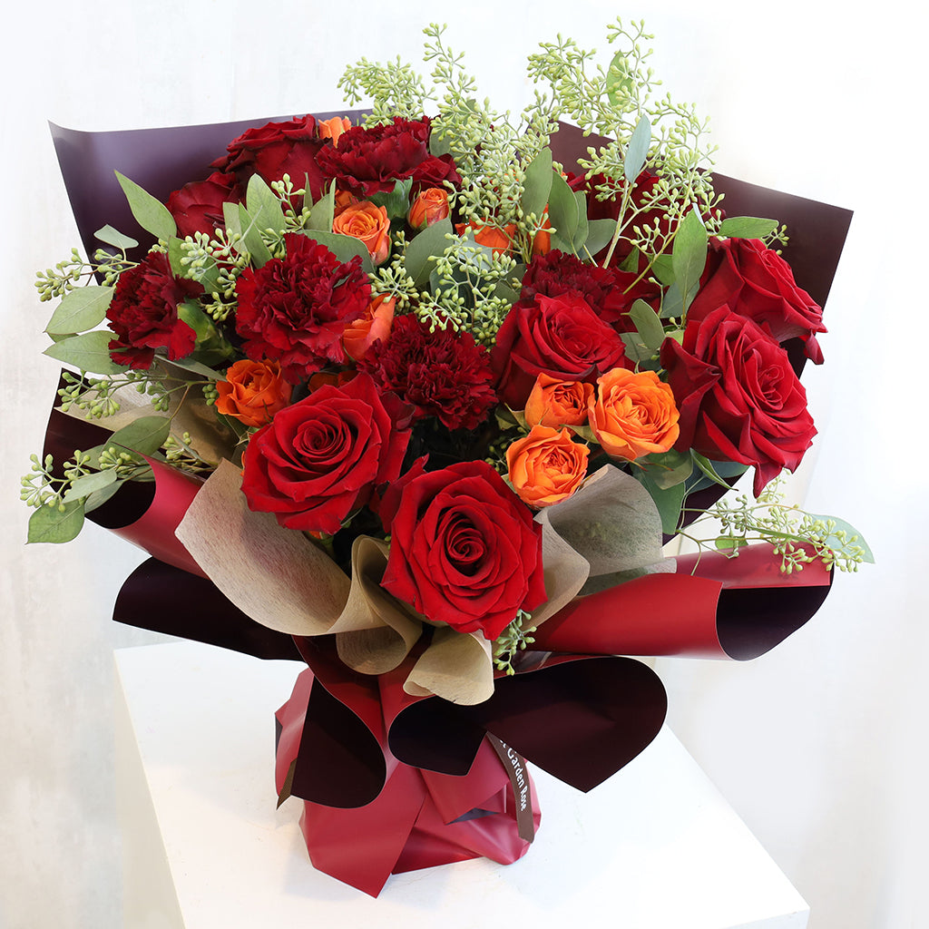 Bouquet of premium red freedom roses carnations and orange spray roses with seeded eucalyptus greeneries.