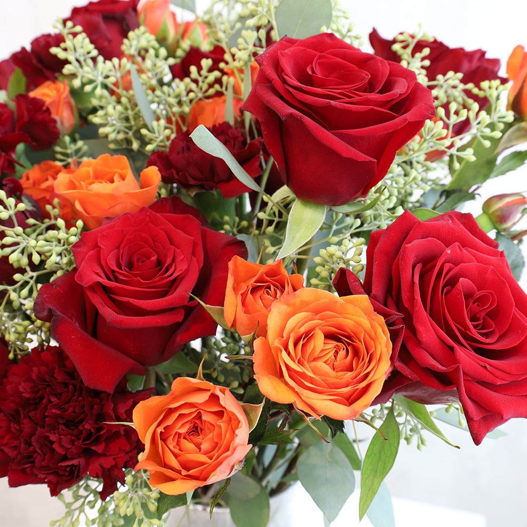 Bouquet of premium red freedom roses carnations and orange spray roses with seeded eucalyptus greeneries.